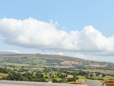 A rural landscape with green fields trees and hills under a blue sky with clouds at Heather Hut at Copy House Hideaway in Earby