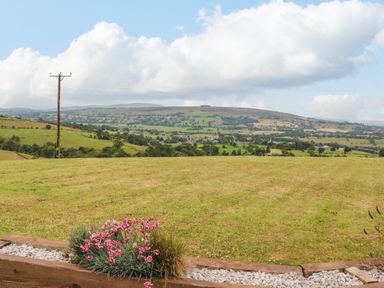 A grassy field with flowers in a wooden planter and hills in the background at Heather Hut at Copy House Hideaway in Earby