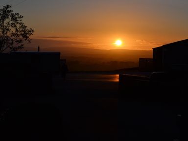 A sunset over a rural area with silhouetted buildings and a tree at Heather Hut at Copy House Hideaway in Earby