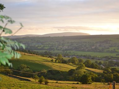A rural landscape with rolling green hills trees and scattered houses at Heather Hut at Copy House Hideaway in Earby
