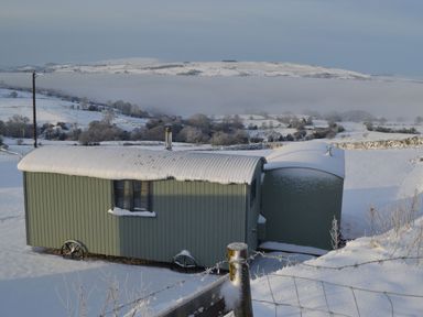 A green shepherd hut covered in snow in a snowy rural landscape at Heather Hut at Copy House Hideaway in Earby