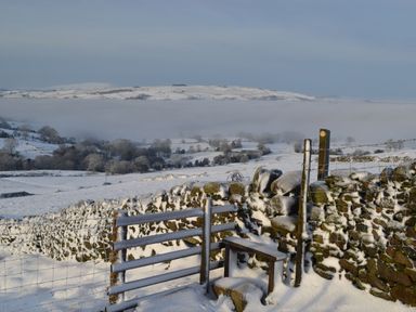 A snowy rural landscape with stone walls a wooden gate and a misty valley at Heather Hut at Copy House Hideaway in Earby