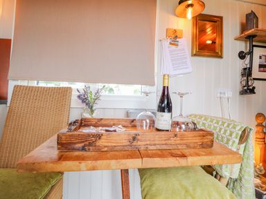 A wooden table with a tray holding a wine bottle and two glasses between two chairs in a room with a window and wall decor at Heather Hut at Copy House Hideaway in Earby