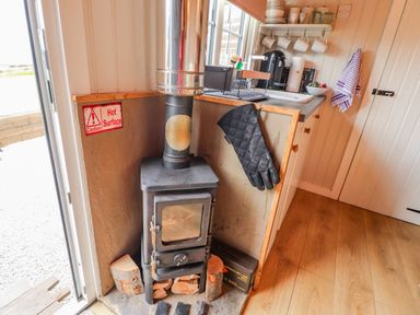 A wood-burning stove next to a kitchen counter with oven mitt hanging and kitchen utensils at Heather Hut at Copy House Hideaway in Earby