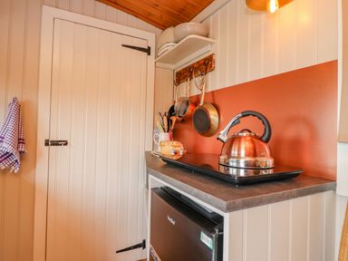A small kitchen area with a kettle on an electric stove hanging pots and pans a loaf of bread and utensils in a holder at Heather Hut at Copy House Hideaway in Earby
