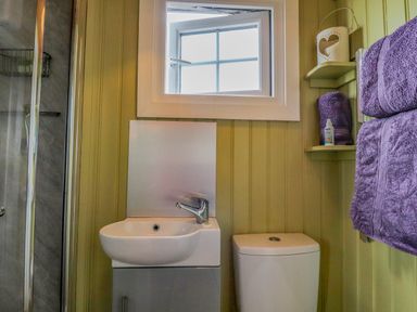 A bathroom with a sink toilet purple towels and a small window at Heather Hut at Copy House Hideaway in Earby