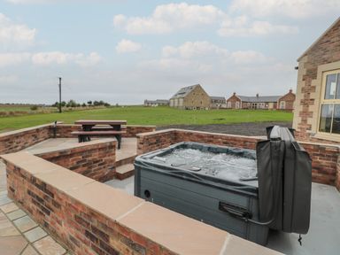 An outdoor patio with a hot tub and a picnic table surrounded by brick walls at Whinny Cottage in Embleton