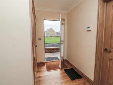 A hallway with wooden floor a partially open door and a black mat at Whinny Cottage in Embleton
