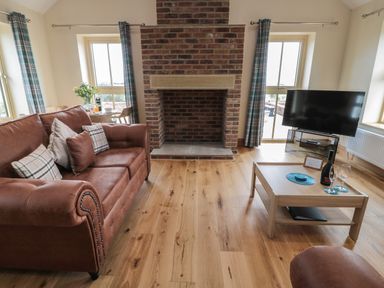 A living room with a brown leather sofa a brick fireplace a wooden coffee table and a TV at Whinny Cottage in Embleton