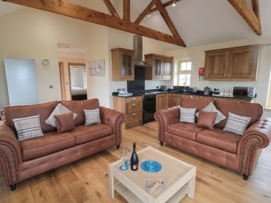 A living room with two brown sofas and a wooden coffee table in front of a kitchen with wooden cabinets at Whinny Cottage in Embleton
