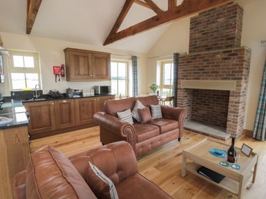 A living room with wooden cabinets leather sofas a brick fireplace and a wooden coffee table at Whinny Cottage in Embleton