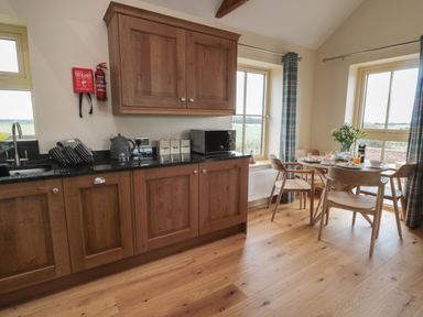 A kitchen with wooden cabinets black countertops and a dining table set with chairs and breakfast items at Whinny Cottage in Embleton