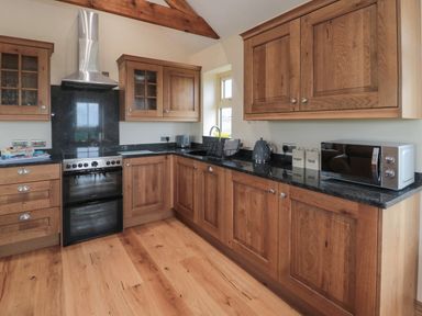 A kitchen with wooden cabinets a black countertop a stove a microwave and a window at Whinny Cottage in Embleton