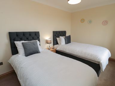 A bedroom with two single beds a bedside table with a lamp and decorative plates on the wall at Whinny Cottage in Embleton