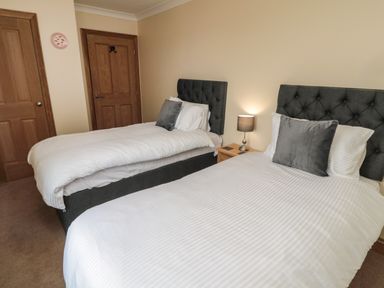 A bedroom with two single beds a bedside table with a lamp and two wooden doors at Whinny Cottage in Embleton