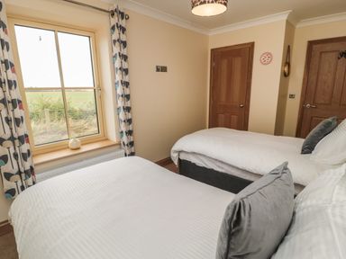 A bedroom with two single beds two wooden doors and a window with patterned curtains at Whinny Cottage in Embleton