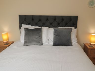 A bedroom with a bed with gray headboard two gray pillows two bedside tables with lamps at Whinny Cottage in Embleton