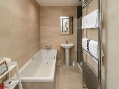 A bathroom with a bathtub sink wall mirror towel rack with towels and a small shelf at Whinny Cottage in Embleton