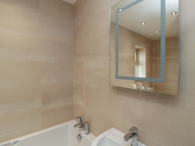 A bathroom with a bathtub, sink, faucet, mirror, and tiled walls at Whinny Cottage in Embleton