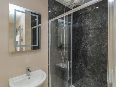 A bathroom with a sink and mirror next to a shower with glass doors and a dark textured wall at Whinny Cottage in Embleton