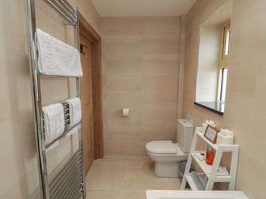 A bathroom with a toilet a towel rack with towels a small shelf holding toilet paper and toiletries at Whinny Cottage in Embleton