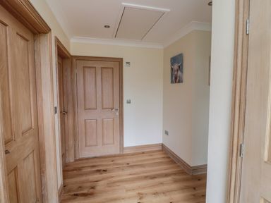 A hallway with wooden doors and hardwood floor and a painting of a cow on the wall at Whinny Cottage in Embleton