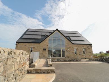 A stone building with large glass windows and solar panels on the roof at Whinny Cottage in Embleton