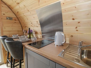A kitchen area with a sink electric kettle cooktop dining setup with plates glasses and chairs at Dysynni Pod in Llanegryn near Tywyn