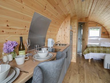 A wooden pod interior with a small kitchen area and dining setup leading to a bed at Dysynni Pod in Llanegryn near Tywyn