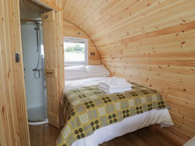 A bedroom with a bed and folded towels near a window and a shower in a wooden pod at Dysynni Pod in Llanegryn near Tywyn