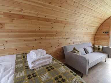 A room with wooden walls a bed with folded towels and a sofa with patterned cushions at Dysynni Pod in Llanegryn near Tywyn