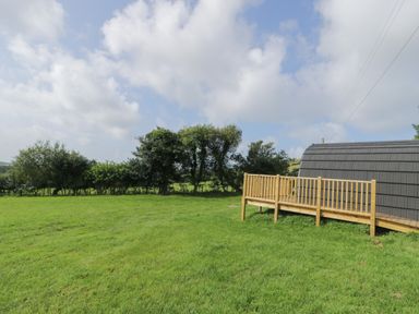 A large grassy field with trees and a wooden deck attached to a pod building at Dysynni Pod in Llanegryn near Tywyn