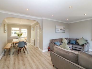 A living room with sofas and cushions connected to a dining area with a wooden table and chairs at Treestumps in Benllech