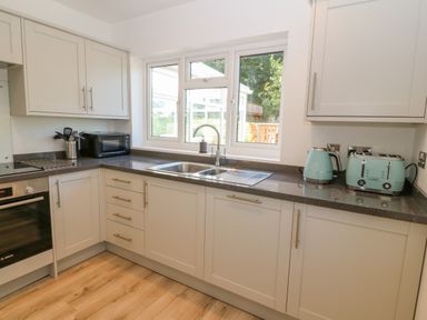 A kitchen with white cabinets black countertop a sink microwave kettle and toaster at Treestumps in Benllech