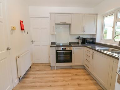 A kitchen with white cabinets a built-in oven a microwave a sink and wooden floor at Treestumps in Benllech