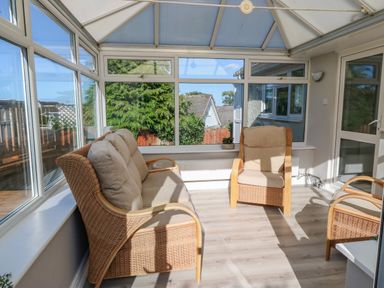 A conservatory with wicker sofa and chairs and large windows at Treestumps in Benllech