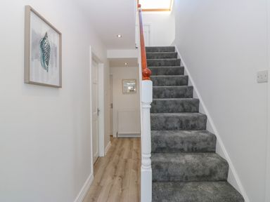 A hallway with wooden floor and a carpeted staircase with white walls at Treestumps in Benllech