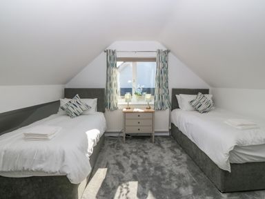 A bedroom with two single beds a bedside table with two lamps and a window with curtains at Treestumps in Benllech