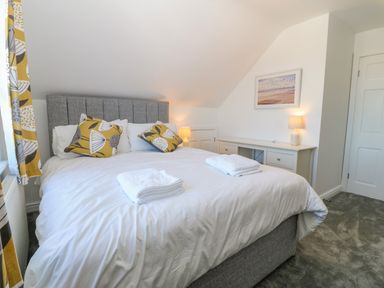 A bedroom with a bed with white bedding and folded towels bedside tables with lamps and a framed picture on the wall at Treestumps in Benllech