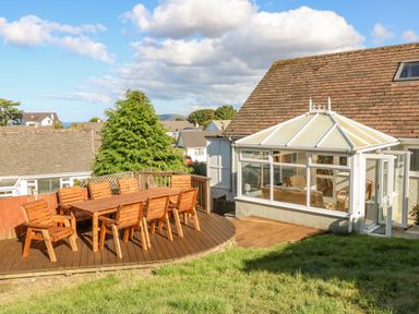 An outdoor wooden deck with table and chairs next to a conservatory at Treestumps in Benllech