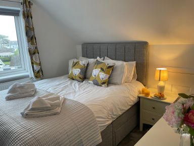 A bedroom with a bed with pillows and folded towels next to a nightstand with a lamp croissants and drinks at Treestumps in Benllech