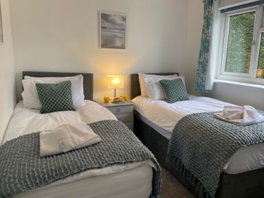 A bedroom with two single beds bedside table with lamp and drinks near a window at Treestumps in Benllech