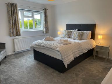 A bedroom with a double bed bedside tables lamps a window with curtains and a grey armchair at Treestumps in Benllech