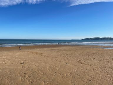 A sandy beach with a few people near the water and hills in the distance at Treestumps in Benllech