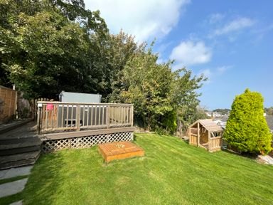 A backyard with grass a wooden deck and a small wooden playhouse at Treestumps in Benllech