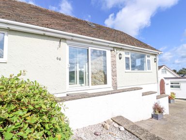 The exterior of a single story house with sliding glass door a window a tiled roof and plants in front at Treestumps in Benllech