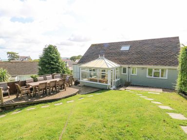 A backyard with a wooden deck and outdoor dining table next to a house with a conservatory at Treestumps in Benllech