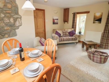 A living room with a dining table set with plates glasses and a wine bottle a sofa with cushions armchair and a window at 2 Yr Hen Felin Castle Morris near Letterston