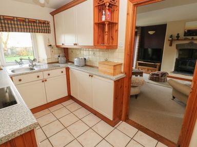 A kitchen with white cabinets and tiled floor adjacent to a living room with a sofa and a fireplace at 2 Yr Hen Felin Castle Morris near Letterston