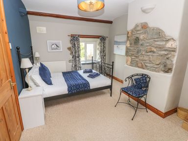 A bedroom with a black metal bed a white bedside table and a chair with blue cushions at 2 Yr Hen Felin Castle Morris near Letterston